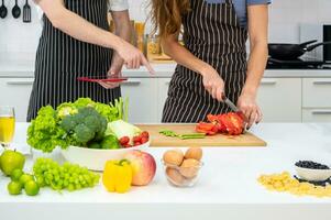 donna taglio verdure con uomo utilizzando tavoletta computer nel cucina a casa foto