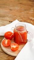 succo di pomodoro in barattolo di vetro e pomodori freschi su fondo di legno foto