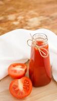 succo di pomodoro in bottiglia di vetro e pomodori freschi su fondo in legno foto