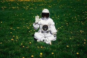 astronauta futuristico in un casco si siede su un prato verde tra i fiori foto