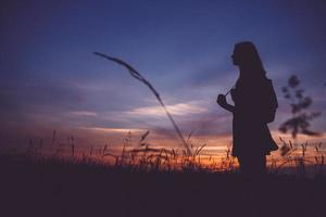 silhouette di una ragazza con uno zaino in un prato sullo sfondo del tramonto foto