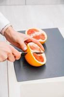 le mani della donna che tagliano il pompelmo fresco sulla cucina foto