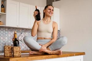 donna in tuta da ginnastica in una cucina leggera beve vino rosso foto