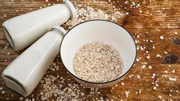 fiocchi d'avena in ciotola bianca e bottiglie di latte fresco foto