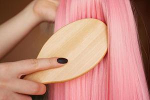 la mano femminile tiene una parrucca rosa con i capelli lunghi e pettina un pettine di legno