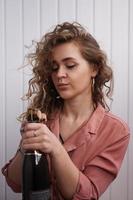 una giovane donna con i capelli ricci apre una bottiglia di champagne foto