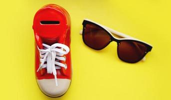 salvadanaio a forma di scarpe da ginnastica. occhiali da sole su sfondo giallo foto