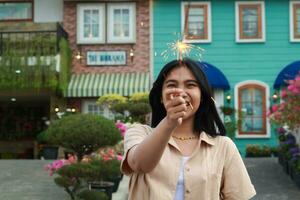 nuovo anno vigilia celebrazione concetto. attraente asiatico giovane donna Tenere sparkler con ridendo contento nel all'aperto giardino di Vintage ▾ Casa cortile foto
