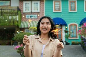 allegro giovane asiatico donna Tenere sparkler per celebrare nuovo anno vigilia con giardino festa in piedi al di sopra di colorato Vintage ▾ Casa cortile foto