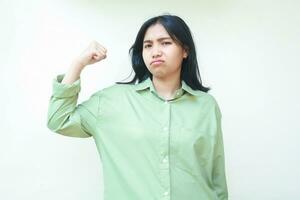 irritato infelice asiatico donna indossare verde sovradimensionato camicia raccolta braccia mostrando bicipite muscolo forza in piedi al di sopra di isolato bianca sfondo, forte e potente fumale insoddisfatto, guardare a telecamera foto