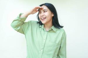 eccitato asiatico donna indossare verde casuale sovradimensionato camicia sorridente Guarda lontano con raccolta mani su fronte in piedi al di sopra di isolato bianca sfondo foto