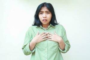 scioccato asiatico donna con buio capelli sembra impaurito con mani toccante il petto indossare verde sovradimensionato camicia isolato su bianca sfondo foto