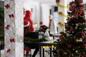 festosamente ornato Natale albero vicino su con uomini d'affari Lavorando nel sfocato sfondo. moderno ufficio con bella natale luci decking il sale durante inverno vacanza stagione foto