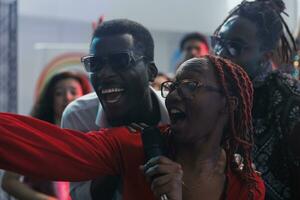 spensierato africano americano donna cantando nel microfono e assunzione autoscatto con amici nel discoteca. allegro sorridente persone ridendo e avendo divertimento mentre in posa per foto nel club