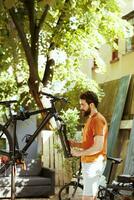 vivace giovane uomo riparazione danneggiato bicicletta ruota con professionale attrezzature nel cortile. dedito salutare caucasico maschio ciclista Lavorando su smontato bicicletta all'aperto per tempo libero Ciclismo. foto