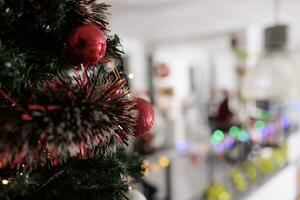 vicino su messa a fuoco su Natale albero decorato nel rosso con moderno ufficio sfocato nel sfondo. ornato professionale posto di lavoro pronto per vacanza stagione segreto Santa aziendale festa foto