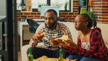 contento vita partner mangiare fette di Pizza su divano, avendo divertimento insieme Guardando preferito film su televisione. giovane uomo e donna nel relazione godendo consegna cibo e alcol. foto