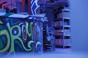 grungy abbandonato camera coperto nel graffiti spray dipingere, opera d'arte illuminato di viola fluorescente luci. urbano abbandonato posto pieno con detriti, distrutto arrugginito magazzino con neon luce. foto