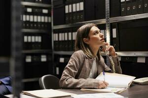 manager parlando a telefono fisso Telefono con a distanza contabile, discutere contabilità rapporto nel Conservazione camera. donna d'affari Lavorando in ritardo a notte a amministrativo Catalogare nel aziendale depositario foto