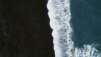 islandese nero sabbia spiaggia aereo Visualizza, spettacolare atlantico riva con onde Crashing su costa. artico scenario con nevoso montagne e nero sabbia su spiagge, freddo paesaggio. lento movimento. foto