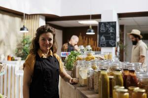 ritratto di sorridente zero rifiuto negozio magazziniere Il prossimo per biodegradabile ecofriendly massa prodotti. gioioso donna Lavorando nel l'ambiente responsabile Locale Quartiere memorizzare foto