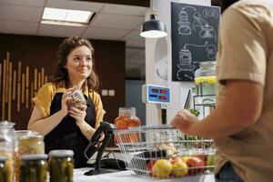 contento donna a check-out contatore nel zero rifiuto negozio vendita salutare Lenticchie nel vaso per vegano cliente con verde vivente stile di vita. cliente acquista cibo nel Locale Quartiere memorizzare a partire dal amichevole venditore foto