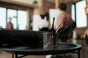 schizzi corso. vicino su di metallo In piedi titolare con grafite matite in piedi su tavolo contro gruppo di persone studenti seduta a cavalletti su sfocato sfondo, studiando disegno nel arte studio foto