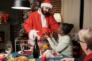 Santa Claus passaggio i regali per persone a festivo cena, diffusione Natale spirito e godendo dicembre festa. persona vestito nel costume e cappello offerta regali per amici e famiglia. foto