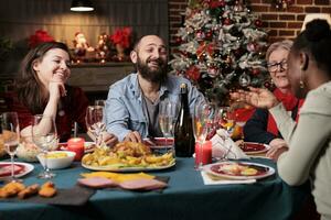 allegro persone parlando e godendo inverno vacanza evento a casa, giovane e vecchio persone avendo divertimento mangiare tradizionale cibo e potabile vino. amici e famiglia raccolta in giro il cena tavolo. foto