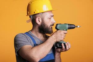 maschio contraente Tenere elettrico perforazione pistola per vite Chiodi e opera su edificio progetto, in piedi al di sopra di studio sfondo. tuttofare costruttore utilizzando cordless energia trapano attrezzo, falegname. foto