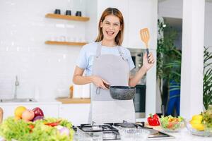 ritratto contento donna cucinando salutare cibo verdura insalata nel cucina con in linea tavoletta foto