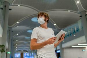 uomo nel respiratore maschera è in attesa Il prossimo aereo a il aeroporto e utilizzando tavoletta. coronavirus covid-19 concetto. foto