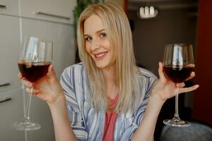 biondo donna tasi Due bicchieri di rosso vino su sua proprio cucina. foto