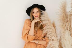 elegante donna nel estate attrezzatura in posa al di sopra di bianca sfondo nel studio con pampa erba arredamento. indossare biancheria vestire. foto