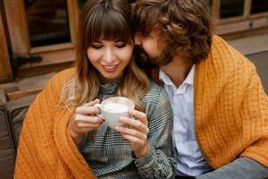 romantico momenti. chilling coppia nel amore seduta su terrazza e potabile mattina caffè e godendo prima colazione. uomo e donna coperto di lenzuolo. foto