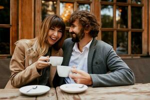 ridendo coppia nel amore. bello uomo con barba e il suo elegante moglie godendo caffè rompere nel bar all'aperto. coppia abbracciare e parlando. foto