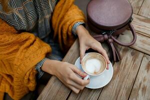 donna potabile caffè . elegante Borsa su tavolo. indossare grigio vestito e arancia plaid. godendo accogliente mattina nel bar. foto