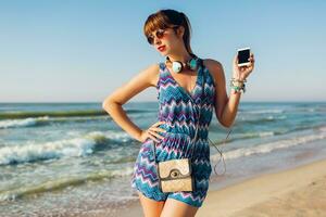 estate soleggiato stile di vita Immagine di giovane donna Tenere mobile Telefono, sms Messaggio , ascoltando preferito musica . indossare di moda estate vestito. foto