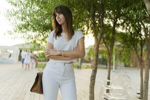 all'aperto ritratto di allegro donna nel bianca maglietta e jeans a piedi nel il parco. foto