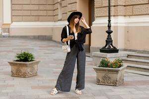 strada moda foto di elegante brunetta donna nel casuale attrezzatura e nero cappello. godendo vacanza nel europeo città. pieno lunghezza.