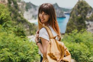 in viaggio e avventura concetto. contento bella donna con indietro imballare in viaggio nel Indonesia su nusa penida isola. sorprendente scogliere e tropicale spiaggia Visualizza su sfondo. foto