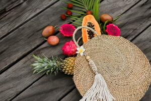 creativo composizione con tropicale frutta nel cannuccia Borsa. superiore Visualizza, legna sfondo, copia spazio. fette di papaia e Drago frutta. palma le foglie. vacanza e vacanza concetto. foto