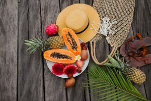 estate tropicale composizione. verde palma le foglie e tropicale frutta su legna sfondo. piatto posizione, superiore Visualizza. cannuccia cappello e uncinetto intrecciata Borsa. foto