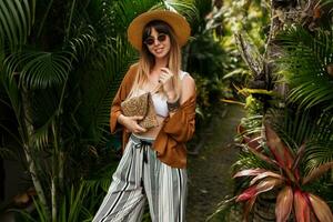 moda Immagine di sexy grazioso donna nel cannuccia cappello in posa su tropicale palma le foglie sfondo nel bali. indossare elegante boemo Accessori. foto