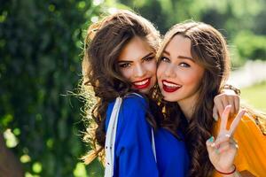 vicino su stile di vita ritratto di Due bella donne abbracci e sorridente. amiche avendo divertimento e l a piedi nel il soleggiato estate parco. indossare casuale attrezzatura . foto