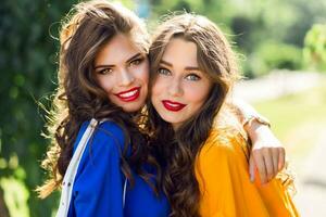 vicino su stile di vita ritratto di Due bella donne abbracci e sorridente. amiche avendo divertimento e l a piedi nel il soleggiato estate parco. indossare casuale attrezzatura . foto