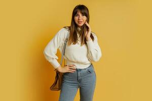 elegante donna in posa nel studio su giallo sfondo. indossare bianca lana maglione e jeans. foto