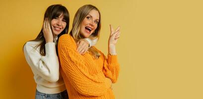 vicino su ritratto di Due bella donna nel accogliente maglioni in posa al di sopra di giallo sfondo. autunno e inverno moda tendenze. foto