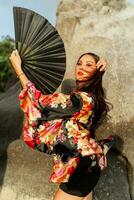bellissimo giapponese donna nel elegante chimono con grande fan e professionale rendere su in posa al di sopra di rocce. foto