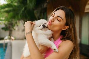 adorabile giocattolo volpino cane nel braccia di suo amorevole proprietario. piccolo adorabile cagnetto con divertente pelliccia con bella donna. tropicale Moder villa su sfondo. foto